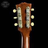 Close-up of the headstock of a vintage Gretsch acoustic guitar against a solid black background, showing the wood grain and tuning pegs.