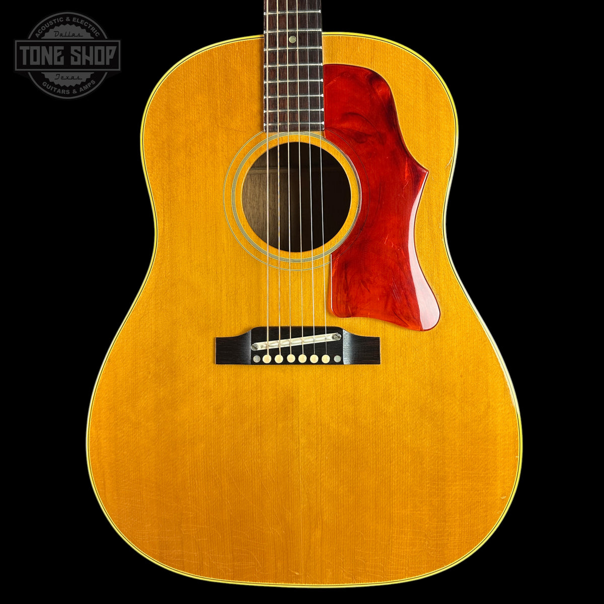 An acoustic guitar with a natural wood finish and a glossy red pickguard, shown against a solid black background with a Tone Shop watermark in the top-left corner.