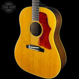 A classic acoustic guitar with a natural wood finish and a dark red pickguard, shown against a solid black background with a Tone Shop watermark in the top left corner.