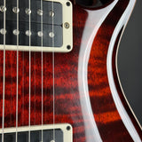 Close-up of an electric guitar body showing a glossy red cherry wood finish with black pickups and cream trim.