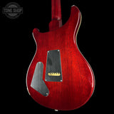 Close-up of the back of a red electric guitar body with a glossy red finish, black pickguard, and gold hardware, shown against a black background with a Tone Shop watermark in the upper left.
