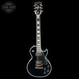 Black electric guitar with gold hardware on a black background, featuring the Tone Shop logo.