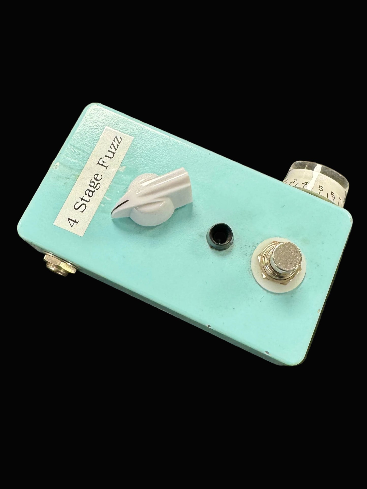 Turquoise guitar effects pedal with knobs on a textured surface