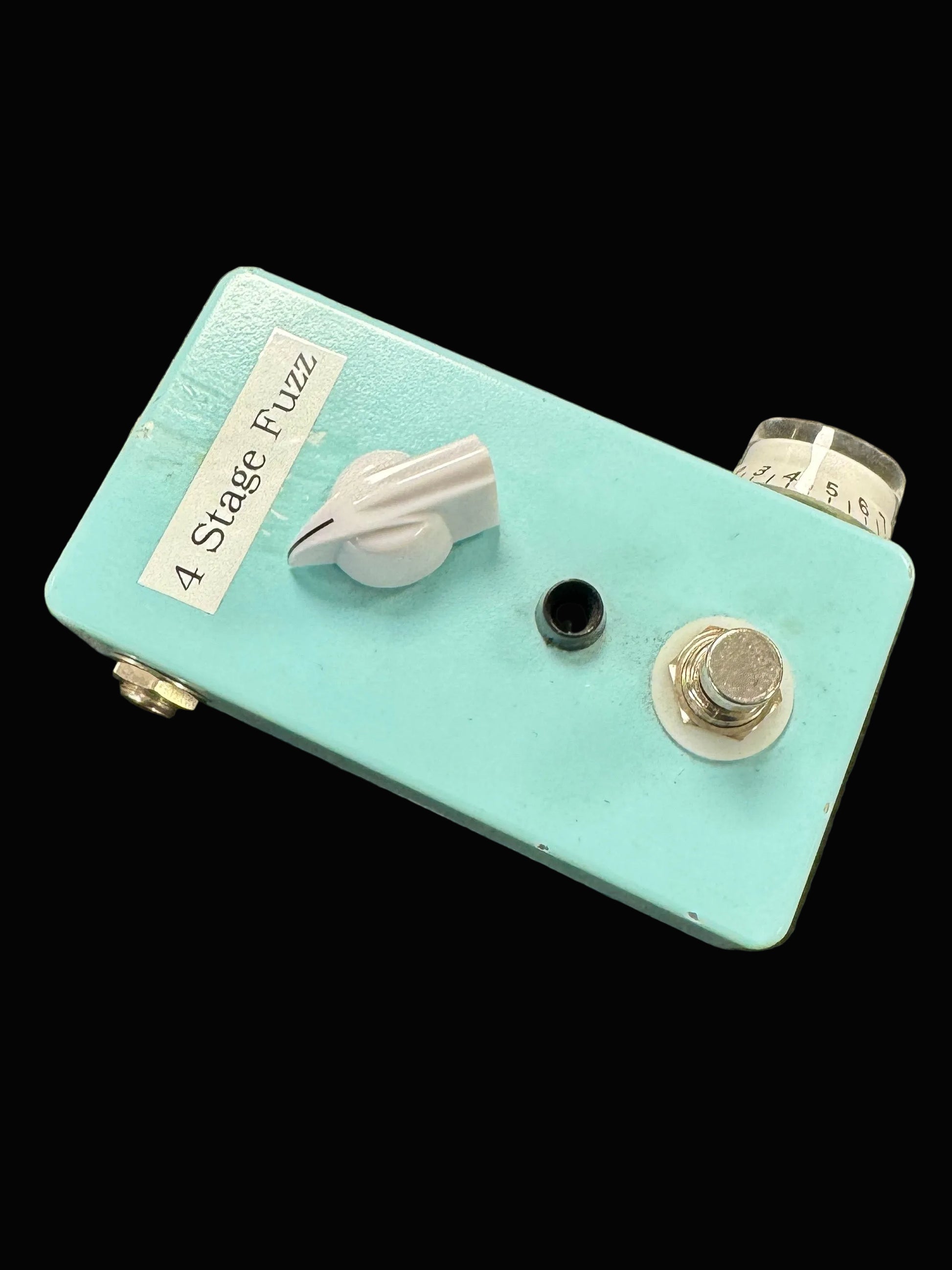 Turquoise guitar effects pedal with knobs on a textured surface