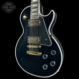 Black electric guitar with gold hardware on a black background, featuring 'Tone Shop' logo.
