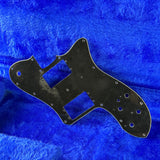 Black guitar pickguard on a blue textured background