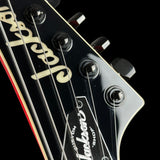 Close-up of a black electric guitar headstock with six tuning pegs, white script branding, and strings against a black background.
