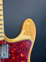 Close-up of a guitar's neck and tortoiseshell pickguard against a dark background