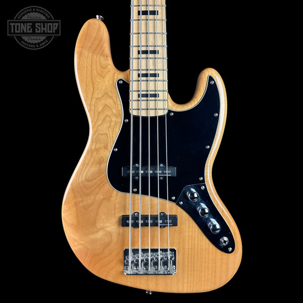A natural wood five-string electric bass guitar with a black pickguard and chrome hardware, shown against a solid black background with a Tone Shop watermark in the top left corner.