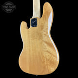 The back of a natural wood electric guitar with a glossy finish, showing a prominent maple top with beautiful grain patterns and a black pickguard, set against a solid black background.