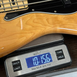 Close-up of a light natural wood bass guitar body resting on a digital scale displaying 10.56 lbs.