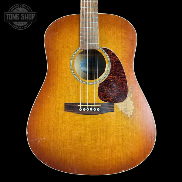A vintage acoustic guitar with a natural sunburst finish, shown from the front against a solid black background. The guitar has a dark pickguard and a visible wear patch on the lower right side of the body.
