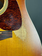 Close-up of an acoustic guitar body showing the natural wood grain sunburst, a dark brown tortoiseshell pickguard, and part of the dark fretboard.