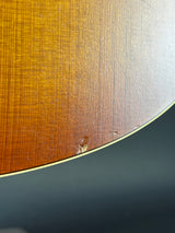 Close-up of a curved wooden surface with a warm brown-to-golden gradient finish and a small visible imperfection near the center, against a dark gray background.
