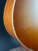 Close-up of the back of an acoustic guitar showing the warm brown wood grain finish and the light cream-colored edge binding against a dark background.