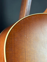 Close-up of a wooden acoustic guitar body showing the grain pattern and a light-colored binding edge against a dark background.