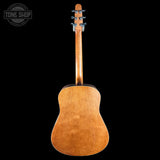 The back view of a wooden acoustic guitar against a solid black background, featuring a warm natural wood finish and a Tune Shop watermark in the top left corner.