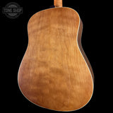 Close-up of the back of an acoustic guitar showing a natural wood grain finish, with a Tone Shop watermark in the top left corner against a black background.