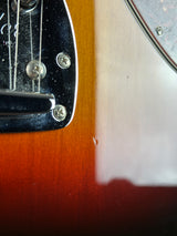 Close-up detail of an electric guitar body showing a sunburst finish, chrome hardware, and strings.