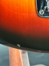 Close-up of a sunburst electric guitar body showing the red-orange fading to black around the edge, with part of a chrome hardware plate visible.