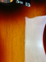 Close-up of a sunburst electric guitar body showing the wood grain finish and part of the black pickguard.