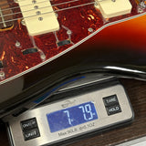 Close-up of a guitar body resting on a digital scale, showing part of the instrument with a red and amber gradient finish and a silver scale displaying the weight.