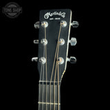 Close-up of the headstock of a Martin & Co. six-string acoustic guitar against a solid black background, showing the brand name in white script and six silver tuning pegs.
