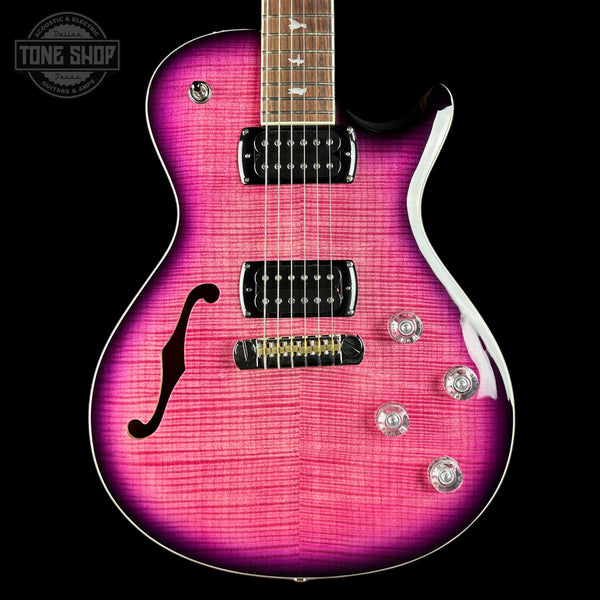 Pink electric guitar with a black pickguard on a black background, featuring the Tone Shop logo.