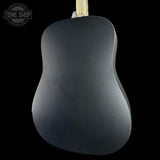 The back of a matte black acoustic guitar, showing its smooth body and the neck at the top against a solid black background.