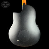 The back of a black electric guitar with a textured metallic black finish, featuring a circular speaker cutout and a small silver screw, shown against a solid black background with a Tone Shop watermark in the top left.