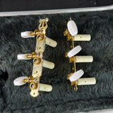 A pair of vintage six-string electric guitar headstocks with ornate gold-tone metal bodies, white bone-style tuning pegs, and small dark gemstone accents, displayed on a black felt surface.