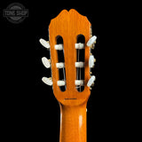 Close-up of the headstock of a classical guitar with six white tuning keys and gold-toned tuners, shown against a solid black background. A Tone Shop watermark is visible in the top left corner.