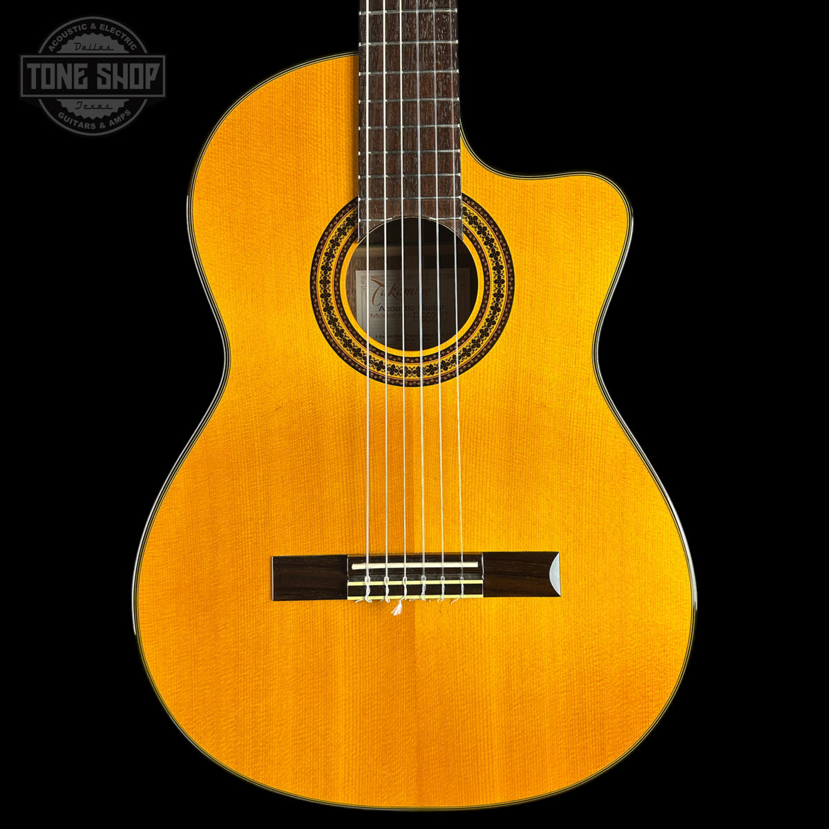 A classical-cutaway acoustic guitar with a natural golden-yellow spruce top, dark fretboard, and black pickguard, shown against a solid black background with a Tone Shop watermark in the top left corner.