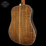 Back view of a wooden acoustic guitar with a visible brand logo in the corner.