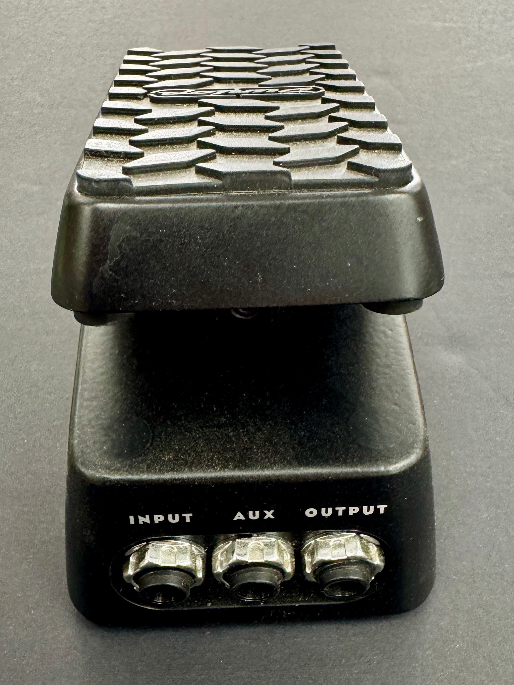 Black guitar effects pedal with textured top and labeled inputs on a gray background