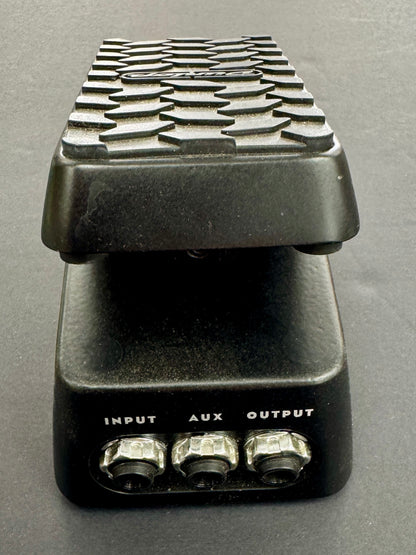 Black guitar effects pedal with textured top and labeled inputs on a gray background