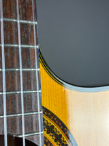 Close-up detail of an acoustic guitar showing the dark brown wooden fretboard, silver metal strings, and the natural wood body with a black soundhole surround.