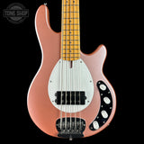 Electric bass guitar with a rose gold body and white pickguard on a black background.