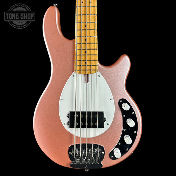 Electric bass guitar with a rose gold body and white pickguard on a black background.
