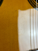 Close-up of an acoustic guitar body showing the natural wood grain, sound hole rosette edge, and six strings.