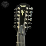 Close-up of a Taylor acoustic guitar headstock with silver tuning pegs and strings against a black background, featuring a Tone Shop watermark in the upper left corner.