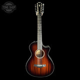 A Taylor acoustic-electric guitar with a dark brown wood finish and cutaway body, shown against a solid black background with a Tone Shop watermark in the top-left corner.