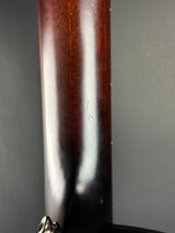 Close-up of a dark brown wooden rifle stock with a glossy finish, showing a white reflection and a small etched marking, set against a dark gray background.