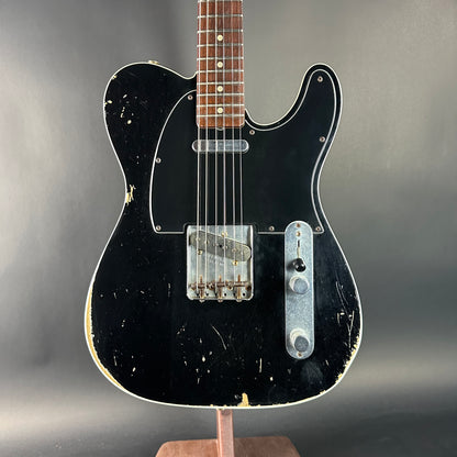 Black electric guitar on a stand against a gray background