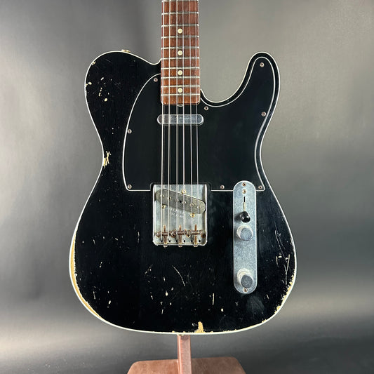 Black electric guitar on a stand against a gray background