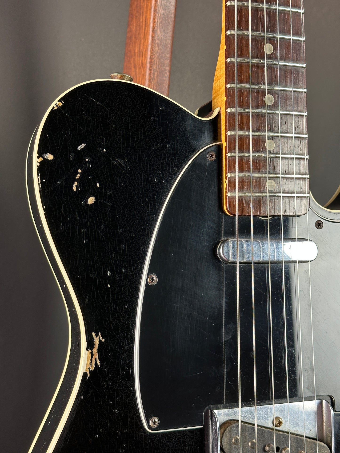 Close-up of a black electric guitar with a worn finish on a dark background