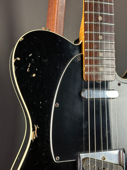 Close-up of a black electric guitar with a worn finish on a dark background