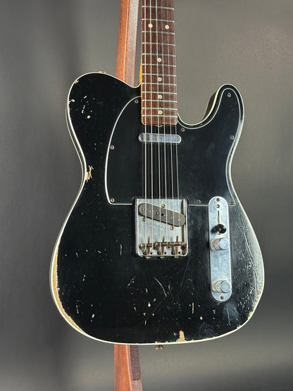 Black electric guitar with a worn finish on a dark background