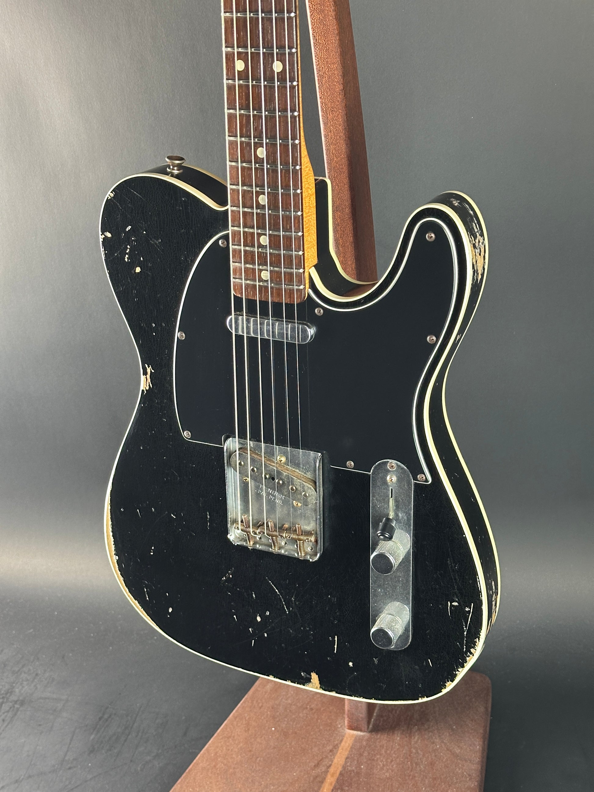 Black electric guitar with a worn finish on a gray background