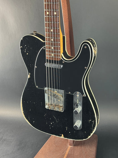 Black electric guitar with a worn finish on a gray background